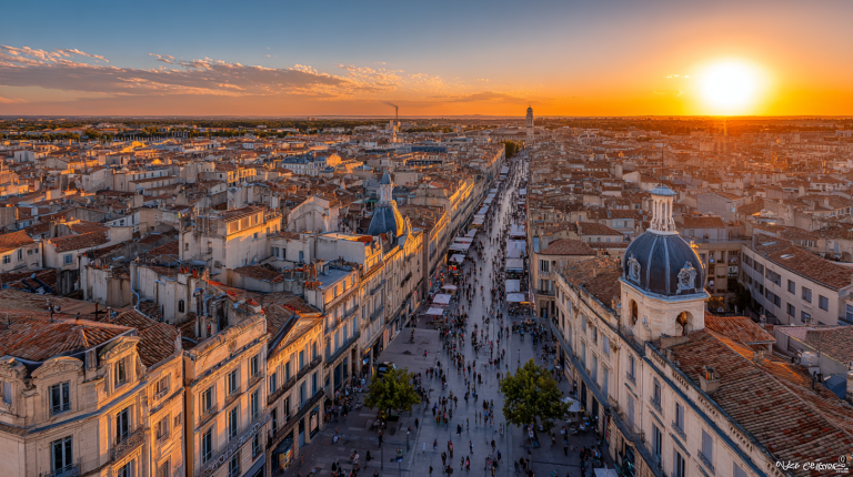 Vue aérienne dynamique de Montpellier au coucher du soleil, mettant en valeur ses bâtiments modernes et historiques dans une ambiance jeune et énergique.